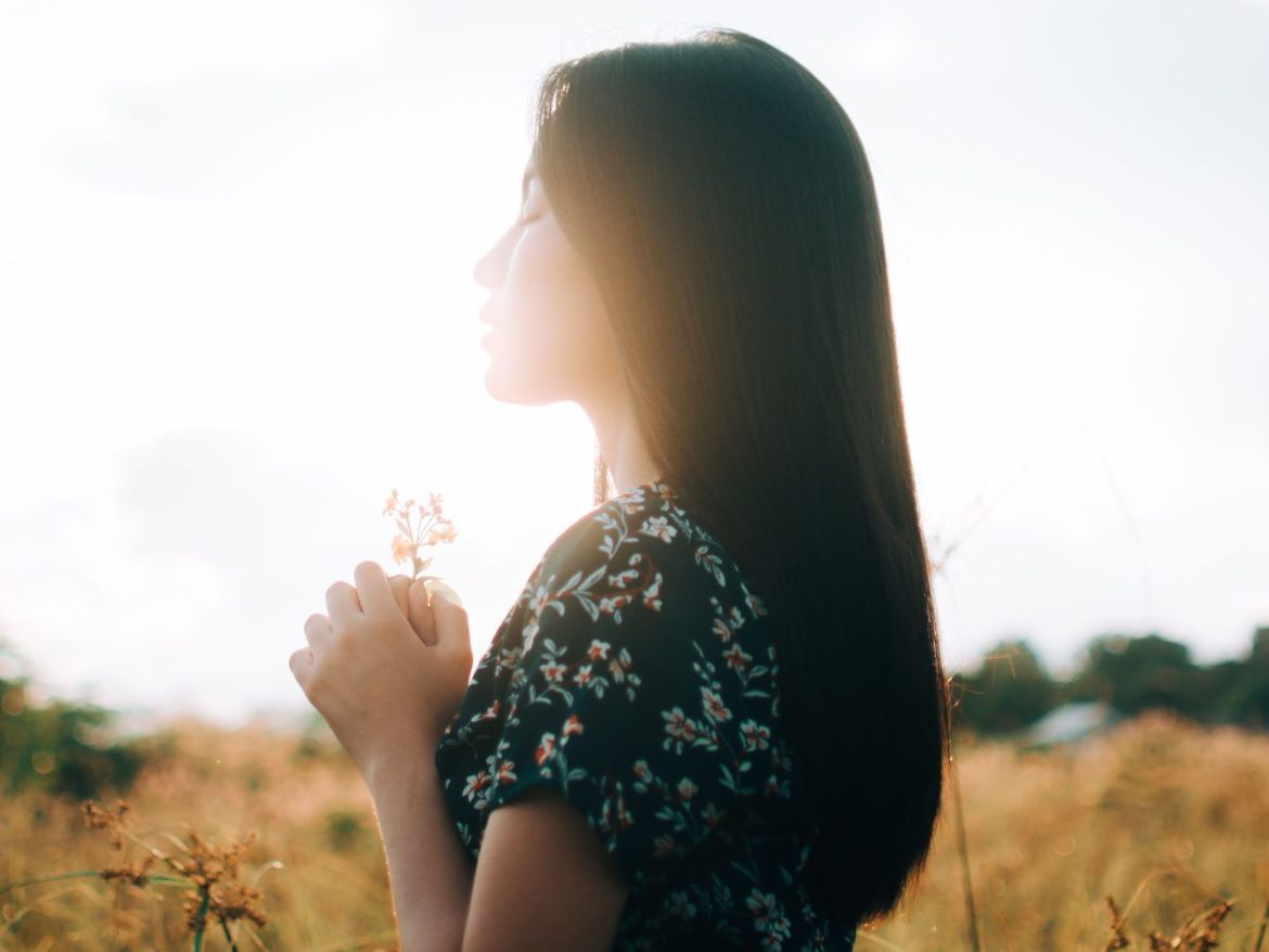 Hopeful woman inhales a flower peacefully with the sun beaming behind her, its a hopeful image